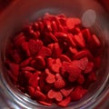 Candy sprinkles in shape of red hearts in glass on background.