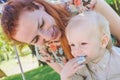 Candy-table. Baby boy eat birthday cake with hands. His mother take him. Birthday party in park on picnic.