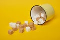 Cane brown and white sugar cubes dropped out of yellow cup on yellow background Royalty Free Stock Photo