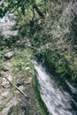 Cane and trekking shoes resting beside mountain water stream fr