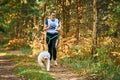 Canicross cross country running with dog, female musher running with Samoyed dog, sled dog racing