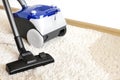 Canister modern vacuum cleaner blue for cleaning the house on the background of a soft beige carpet.