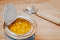 Canned freshly opened corn grain close-up in a jar and juice with an opener on a wooden table