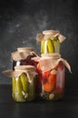 Canned fruits and vegetables, plum, cucumber, tomato in glass jars on black wooden board.