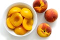 Canned peach halves in bowl on white background with whole fresh Royalty Free Stock Photo