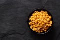 Canned sweet corn in a black ceramic bowl isolated on black slate. Top view. Space for text