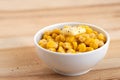 Canned sweet corn with a knob of butter and ground black pepper in a white ceramic bowl isolated on light wood. Space for text