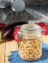 Canned white beans in a glass jar. On a wooden table are pockmarked with beans peppers and eggplant. Close-up