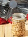 Canned white beans in a glass jar. On a wooden table are pockmarked with beans peppers and eggplant. Close-up