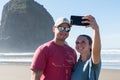 A young couple of tourists make selfies in front of the Haystack Rock in Cannon Beach, Oregon, USA. Royalty Free Stock Photo