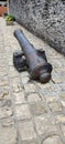 a cannon on cobblestones in front of a fortified castle