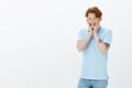 Cannot hide happiness inside. Jyful excited cute guy with red hair, holding palms on cheeks and smiling broadly, feeling