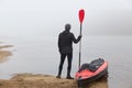 Canoe tour on a river, sportsman posing backwards with oar near red boat, man looking at foggy water, wants rowing boat, enjoying Royalty Free Stock Photo