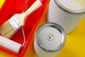 Cans of orange paint, brush, roller and container on yellow background, closeup Royalty Free Stock Photo
