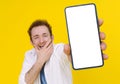 Cant believe, shocked young man with smartphone showing a white empty screen isolated over yellow game, bet, lottery win