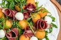 Cantaloupe melon with prosciutto or jamon, mozzarella and green basil leaves, traditional Spanish and Italian appetizer, top view