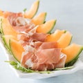 Cantaloupe wedges wrapped in prosciutto on a bed of arugula leaves.