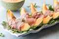 Cantaloupe wedges wrapped in prosciutto deli meat on a bed of arugula.