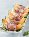 Cantaloupe wedges wrapped in prosciutto on a platter of arugula.
