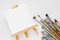 Canvas on easel, paint tubes and bundle of brushes for painting Royalty Free Stock Photo