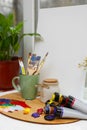 Canvas, wooden artist\'s palette with colorful paints and brushes on white table near window