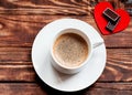 Cap of coffee with foam, two chocolates on red heart on the wooden table.  Flat Lay with no people Royalty Free Stock Photo