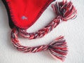 Cap with earflaps in the Norwegian style. Knitted fashion item with ties and pom-pom tassels. Red yarn with black and Royalty Free Stock Photo