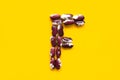 Capital letter F from dry uncooked red and white speckled beans legumes on bright yellow background. Creative food typography art
