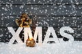 Capital letters forming the word xmas golden putto figurine and candle on pile of snow against wooden wall snow is falling Royalty Free Stock Photo