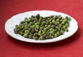 Capper. Green capers in a plate in red blurry background. Fresh cappers in a white plate