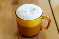 Cappuccino in a clear amber glass mug, with foam visible on top and layers visible through the glass