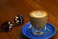 Cappuccino coffee latte art, Warm coffee in clear glass on blue plate with blurred eyeglasses background.