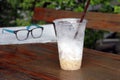 Less cappuccino coffee in the plastic cup and out focus spectacles on the newspaper on the wooden table. Royalty Free Stock Photo