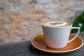 Cappuccino coffee in white cup on wooden table with old brick wa Royalty Free Stock Photo