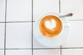 Cappuccino cup on tiled white table background. Foam is decorated with cinnamon heart. Copy space. Top view.