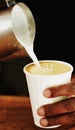 Cappuccino goodness on the go. a barista pouring frothed milk into a take away cup.