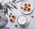 Cappuccino or latte with milk foam in a cup with homemade berry cookies and blueberries on a light background with eucalyptus