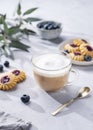 Cappuccino or latte with milk foam in a cup with homemade berry cookies and blueberries on a light background with eucalyptus
