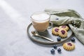 Cappuccino or latte with milk foam in a cup with homemade berry cookies and blueberries on a light background with gypsophila