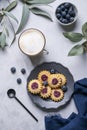 Cappuccino or latte with milk foam in a cup with homemade berry cookies in a dark plate and blueberries on a light background