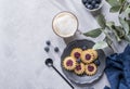 Cappuccino or latte with milk foam in a cup with homemade berry cookies in a dark plate and blueberries on a light background