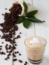 Cappuccino or latte with milk froth in a glass. ÃÂ¡offee beans in a bag of coffee and coffee leaves on a white wooden background. Royalty Free Stock Photo