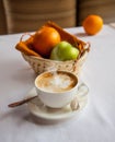 Cappuccino photo. Basket with fruits and coffee with a small cake and a spoon.