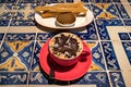 A cappuccino red cup with a plate with churros and dulce de leche - caramel on a coffee shop table