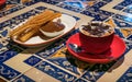 A cappuccino red cup with a plate with churros and dulce de leche - caramel on a coffee shop table