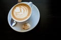 Cappuchino or latte coffe in a white cup with heart shaped foam on wooden board. Morning energy dring isolated on dark