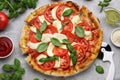 Delicious Caprese pizza with tomatoes, mozzarella and basil on light grey table, flat lay