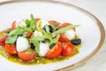 Caprese salad with fresh cherry tomatoes mini mozzarella pesto basil olive oil and balsamic sauce on a white plate and on a Royalty Free Stock Photo