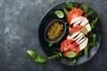 Caprese salad. Italian caprese salad with sliced tomatoes, mozzarella cheese, arugula, basil, olive oil in black plate over old br Royalty Free Stock Photo