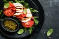 Caprese salad. Italian caprese salad with sliced tomatoes, mozzarella cheese, arugula, basil, olive oil in black plate over old br Royalty Free Stock Photo